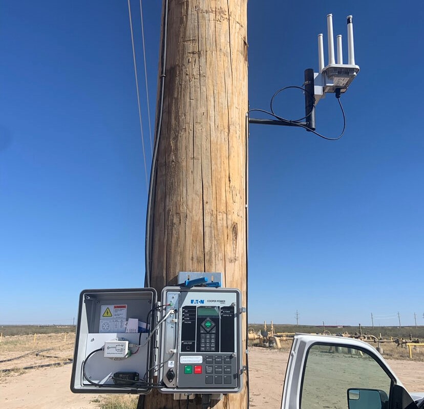 Wireless access point and Eaton Cooper Power control cabinet mounted on a utility pole at a remote field site, with a service truck parked alongside