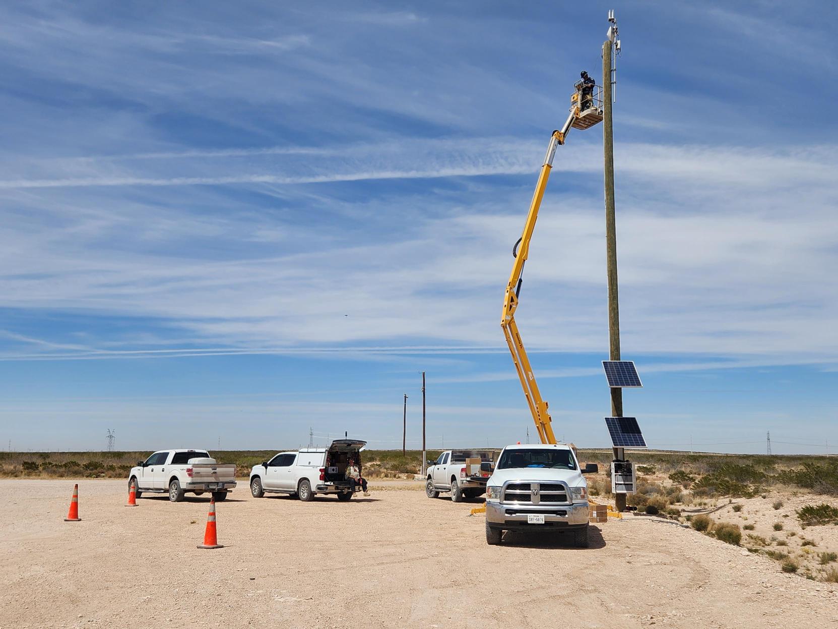 Twin Eagle field crew operating a manlift on a communications tower with field trucks staged on a Permian Basin lease road