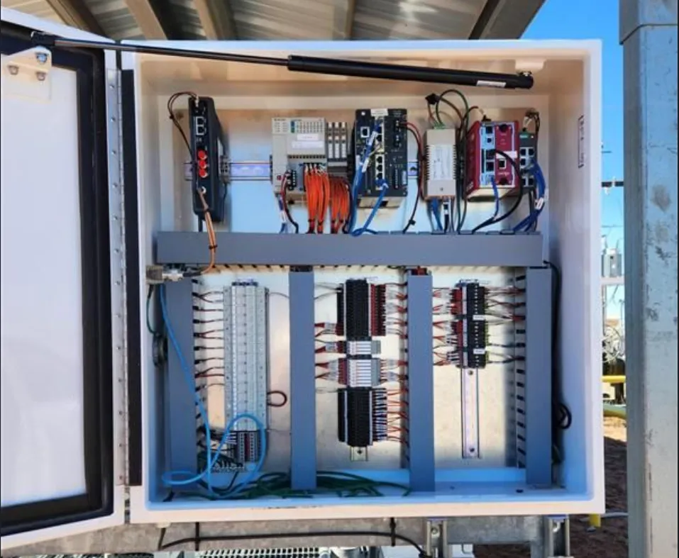 Open NEMA enclosure showing Twin Eagle's hardened wireless and routing hardware deployed at a remote pad — switches, radios, and terminal blocks neatly racked and wired