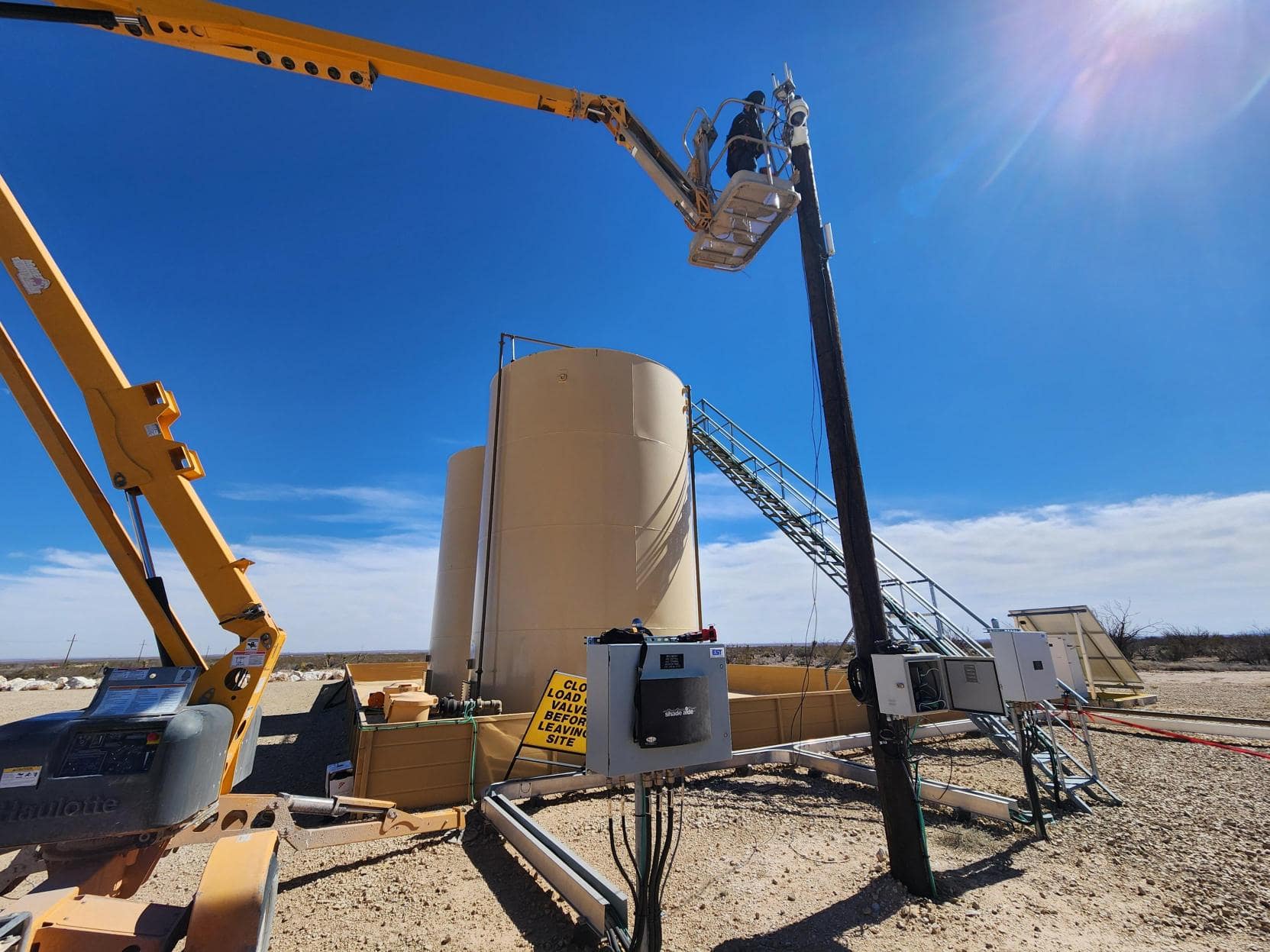 Twin Eagle field engineer working from a man-lift to service a tank-side communications and instrumentation panel at a remote oilfield site