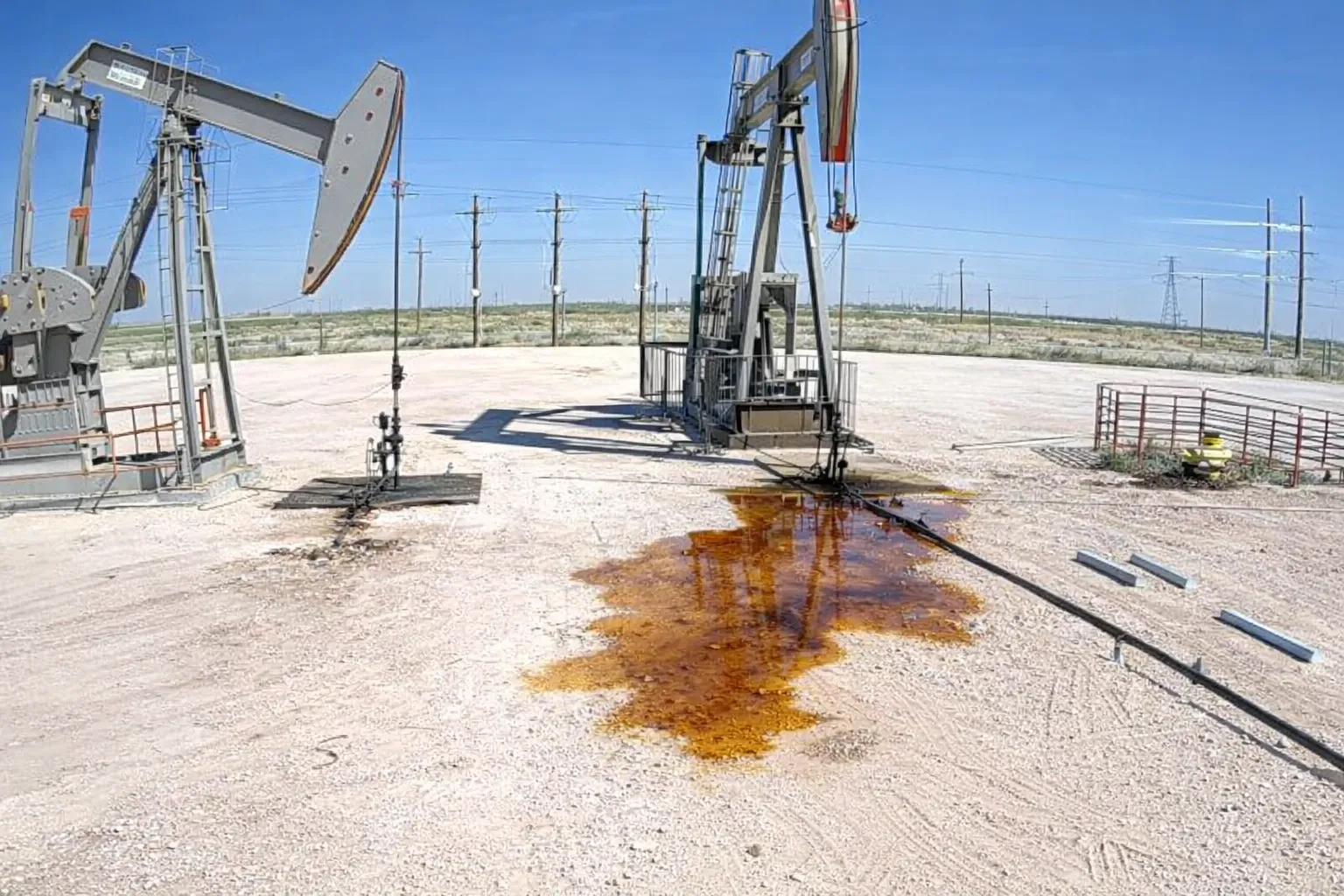 Raw camera frame from a stripper-well pad showing pooled liquid near the pumpjack